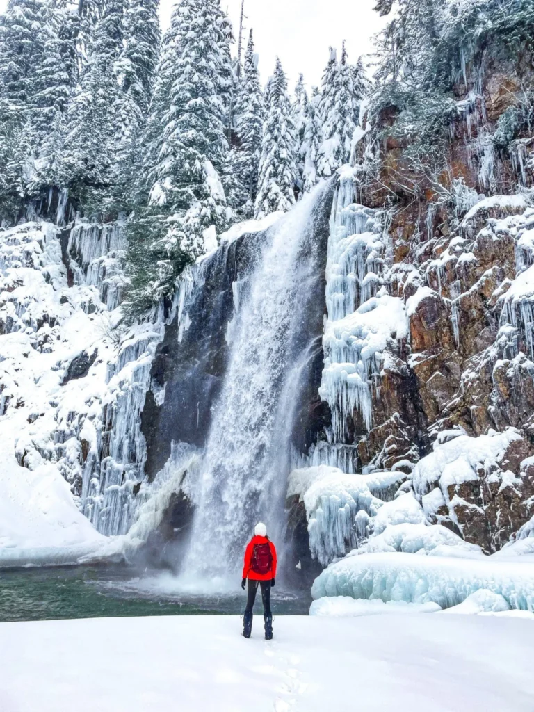 A mountaineer wearing a red jacket is standing at the foot of frozen Franklin Falls Winter Wonderland.